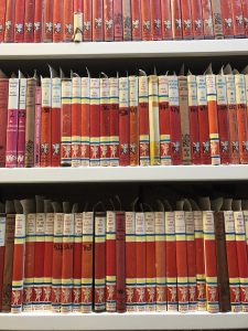 shows three shelves of Mills & Boon books with red spines and Cupid illustration